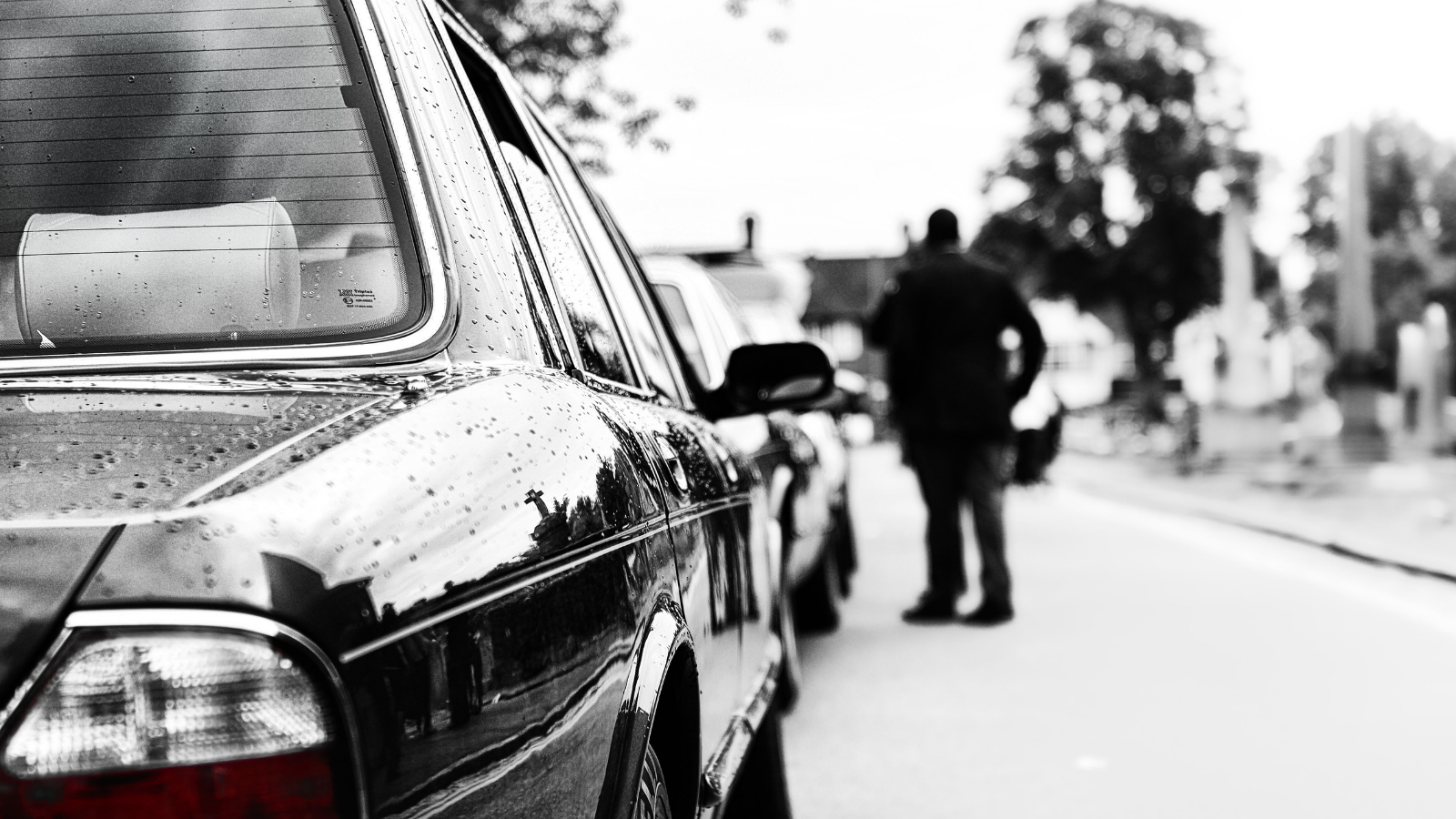 Black and white photo of a person standing next to a car