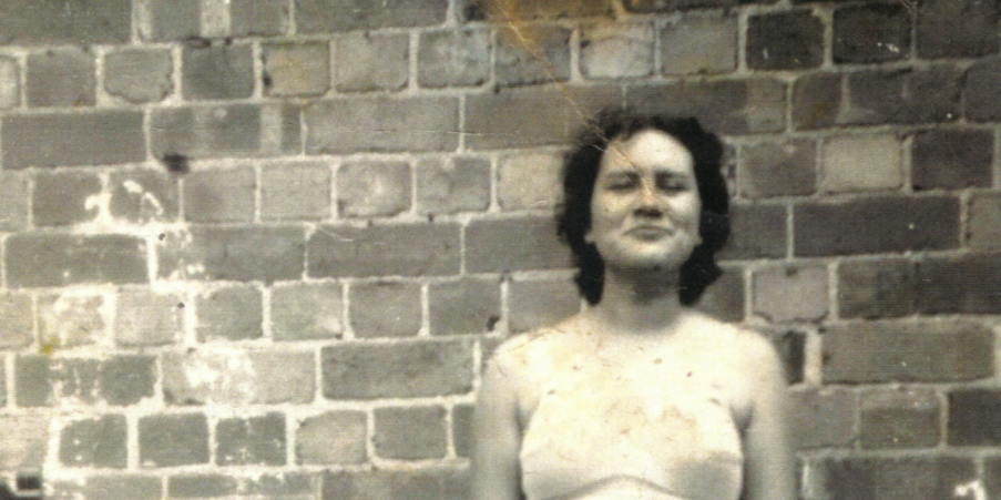 Black and white photo of a young Alma Thorpe standing against a brick wall.