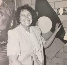 Alma Thorpe stanind in front of an Aboriginal flag. 