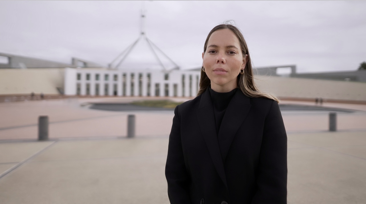 Woman in black turtle neck and brown hair stands in front of Parliment House