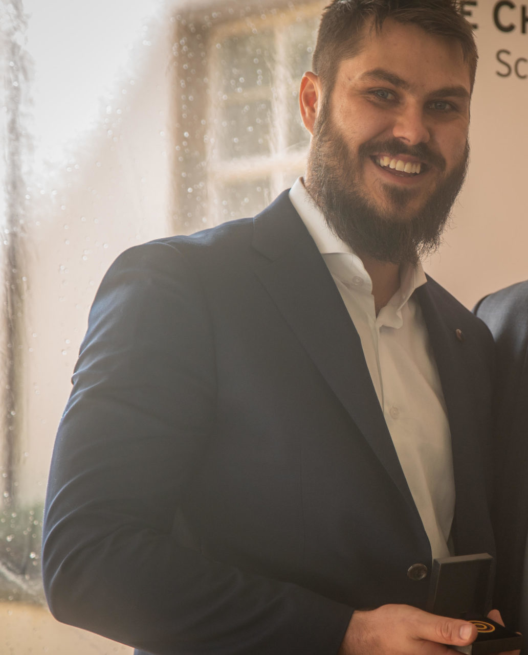 Ethan Taylor stands in a suit with his Charles Perkins award.
