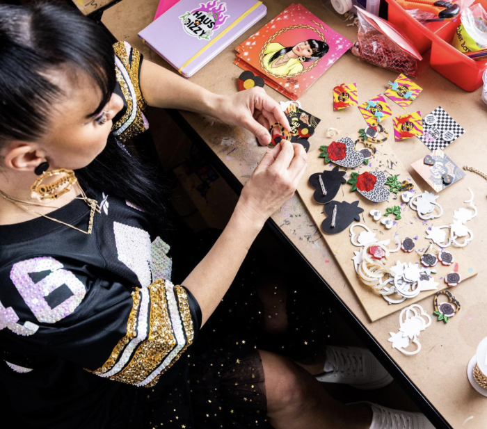 Wiradjuri woman Kristy Dickinson sits at a table making jewelry. It's bright and colourful.