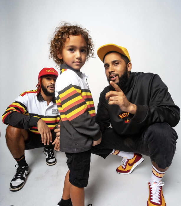 Three First Nations people are wearing bright clothing in red, black and yellow.