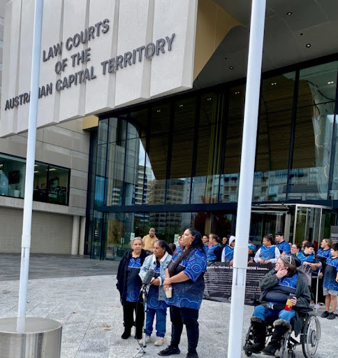A group of people stand before a courthouse. They all wear blue.
